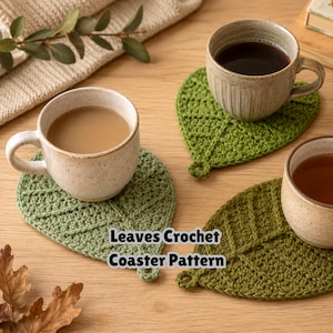 May include: Three leaf-shaped crochet coasters in varying shades of green, each featuring a central vein detail and a small loop at the base. The coasters are topped with ceramic mugs filled with beverages. Text reads: Leaves Crochet Coaster Pattern.