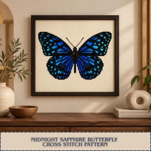 May include: A framed cross stitch pattern featuring a symmetrical butterfly with vibrant blue and black wings. The butterfly is centered on a cream-colored fabric background. The dark brown frame surrounds the square piece of needlework art.