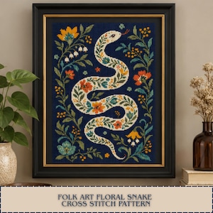 May include: A framed cross stitch artwork featuring a white snake with intricate orange, yellow, and green floral patterns on a dark blue background, surrounded by a border of colourful flowers and leaves, with the text FOLK ART FLORAL SNAKE CROSS STITCH PATTERN.