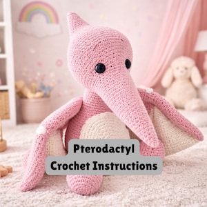 Może przedstawiać: Różowy szydełkowy pterodaktyl z czarnymi guzikowymi oczami i długim dziobem. Skrzydła są w kolorze kremowym. Tekst "Pterodactyl Crochet Instructions" jest wyświetlany na szarym prostokącie.