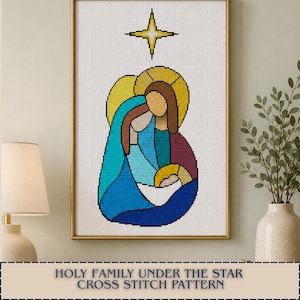 以下が含まれることがあります： HOLY FAMILY UNDER THE STARというタイトルのクロスステッチパターン。青、ターコイズ、紫、黄色の色調で描かれた3人の人物が明るい黄色の星の下に配置され、白いグリッドの背景にゴールドのフレームで囲まれています。