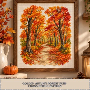 Può includere: Uno schema a punto croce incorniciato che raffigura un sentiero nel bosco fiancheggiato da alberi con fogliame autunnale dai colori arancione, rosso e giallo. L'opera è in una cornice di legno scuro e mostra una scena dettagliata di foglie.