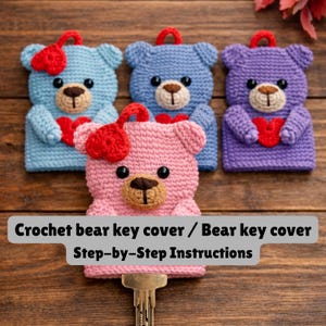 May include: Crocheted bear key covers in blue, pink, and purple, each with a red heart and bow. The covers have brown noses and black eyes. The image includes the text "Crochet bear key cover / Bear key cover Step-by-Step Instructions."