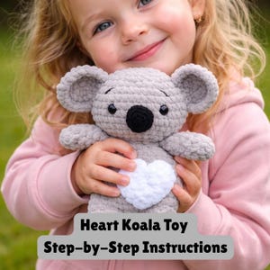 May include: A crocheted gray koala toy with a white heart on its chest is held by a child. The koala has black eyes and a black nose. The text "Heart Koala Toy Step-by-Step Instructions" is at the bottom of the image.