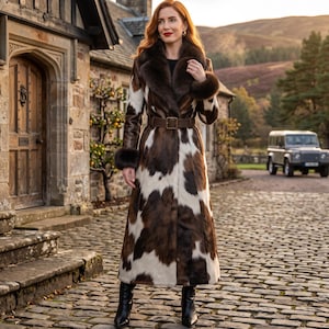 Peut inclure: Un long manteau arrivant aux chevilles avec un motif de taches de vache marron et blanc. Le manteau présente un col en fourrure marron foncé et des poignets assortis. Une large ceinture marron foncé avec une boucle rectangulaire serre la taille.