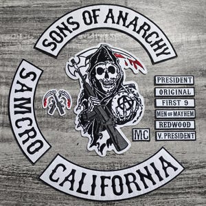 Op de afbeelding: Een verzameling geborduurde patches met de woorden "SONS OF ANARCHY", "SAMCRO" en "CALIFORNIA". De centrale patch toont een Grim Reaper met een geweer. Extra patches bevatten titels als "PRESIDENT" en "ORIGINAL".