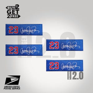 May include: Blue rectangular patches with the number 23 in red and a white signature. The patches are embroidered with white thread. The image also includes the text "BUY 2 GET 2 FREE" and "UNITED STATES POSTAL SERVICE".