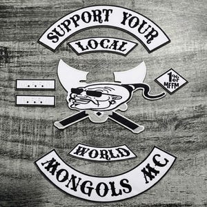 Puede incluir: Un conjunto de parches bordados en blanco y negro. Los parches incluyen las frases "SUPPORT YOUR LOCAL", "WORLD" y "MONGOLS MC". Un parche central presenta un personaje de dibujos animados con gafas de sol y armas cruzadas. Parches adicionales incluyen "1% er MFFM".
