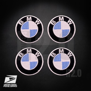 May include: Four circular BMW patches. Each patch features the BMW logo: a black ring with the letters "BMW" in white, surrounding a blue and white checkered center. The patches are on a dark background.