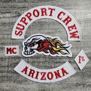Puede incluir: Conjunto de parches bordados con texto rojo sobre tela blanca. Incluye "SUPPORT CREW", "ARIZONA", "MC" y "1%", además de una calavera con llamas. Para entusiastas de las motos.
