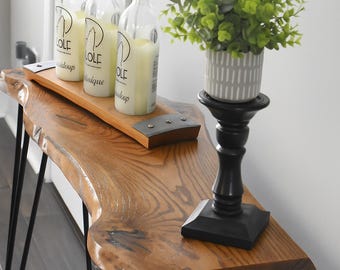 May include: A wooden console table with black hairpin legs. Three clear glass bottles with white candles sit on a wooden tray. A small potted plant in a gray and white striped pot sits on a black candlestick.