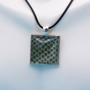 May include: A silver pendant necklace with a square green glass charm featuring a textured pattern. The necklace has a black cord.