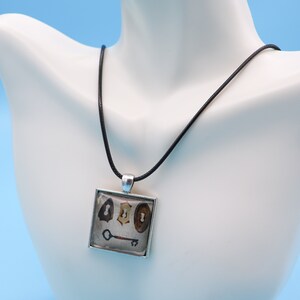 May include: A silver square pendant necklace with a black cord. The pendant features a vintage image of three antique keys and a keyhole.