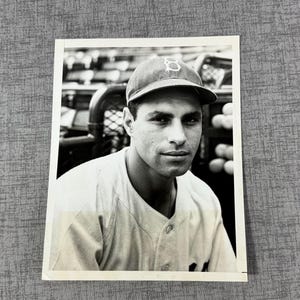 May include: Black and white photo of a baseball player wearing a baseball cap with a "B" on it. The player is wearing a baseball uniform and has a serious expression on his face.