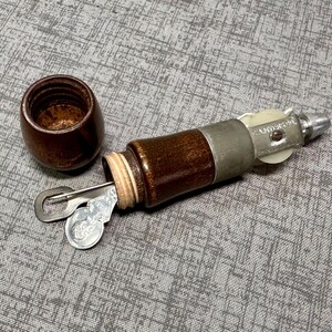 Puede incluir: Un punz&oacute;n de coser de madera con una aguja de metal y un carrete de hilo. El punz&oacute;n est&aacute; en una caja de madera con una tapa de metal.