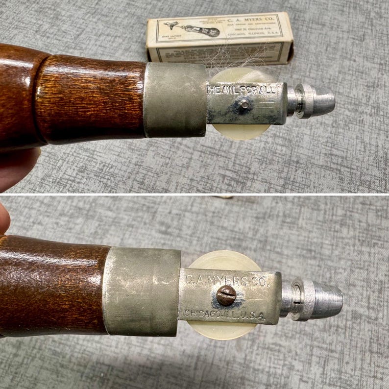 Puede incluir: Primer plano de una herramienta vintage C.A. Myers Co. The Nail-ForAll con mango de madera, carcasa de metal plateado y rueda de pl&aacute;stico blanca. La herramienta se utiliza para clavar clavos en lugares de dif&iacute;cil acceso.