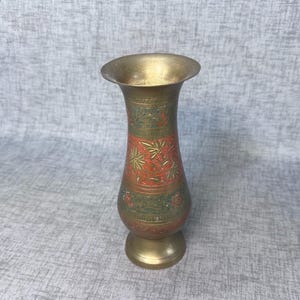 May include: A brass vase with a flared top and a round base. The vase features intricate etched designs in red and green, with a gold-colored finish. The vase is approximately 8 inches tall.