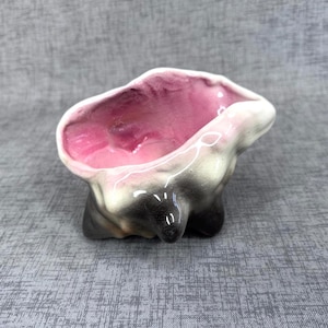 May include: A small, ceramic planter with a unique, organic shape. The interior is a vibrant pink, transitioning to a lighter pink at the rim. The exterior features a gradient of gray and black, creating a striking contrast. The planter has a glossy finish.