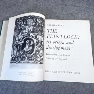 May include: An open book titled "THE FLINTLOCK: its origin and development" by Torsten Lenk. The book has a black and white illustration on the left page and text on the right. Published by Bramhall House, New York.