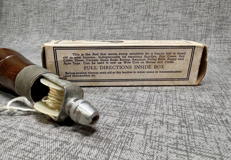 Puede incluir: Un punz&oacute;n de coser de cuero vintage con mango de madera y aguja de metal. El punz&oacute;n est&aacute; en una caja de cart&oacute;n con el texto "This is the Awl that meets every condition for a handy tool to mend old or new harness. Indispensable for repairing Saddles, Gun Cases, Suit Cases, Shoes, Carpets, Grain Bags, Burlap, Awnings, Pulley Belts, Buggy and Auto Tops. Can be used to sew up Wire Cuts on Horses and Cattle. FULL DIRECTIONS INSIDE BOX Before sewing always soak old or dry leather in water same as harnessmakers and shoemakers do."
