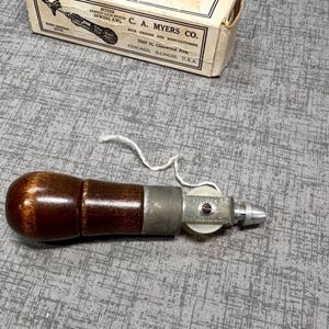 Puede incluir: Un punz&oacute;n de mango de madera marr&oacute;n con un carrete de metal y una aguja de metal. El punz&oacute;n se utiliza para coser cuero.