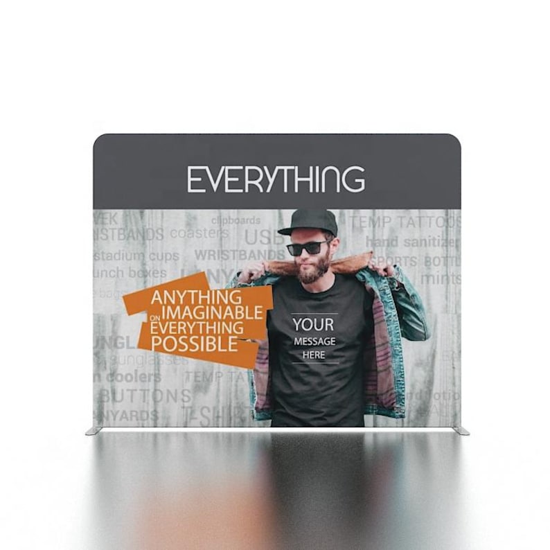 May include: A gray fabric backdrop with the word "EVERYTHING" printed in white. The backdrop features a man wearing a black t-shirt with the text "YOUR MESSAGE HERE" printed in white. The backdrop also features the text "ANYTHING ON IMAGINABLE EVERYTHING POSSIBLE" printed in orange.