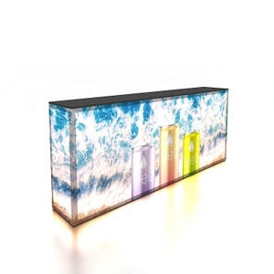 May include: A rectangular display case with a black top and a beach-themed backdrop. The case features three colorful beverage cans with the word "elz" and a water droplet logo. The background depicts ocean waves and sand.
