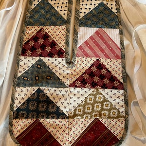 May include: A patchwork quilt with a variety of floral and geometric patterns in shades of red, green, blue, and cream. The quilt is made up of triangles and squares, and it has a simple, rustic look.