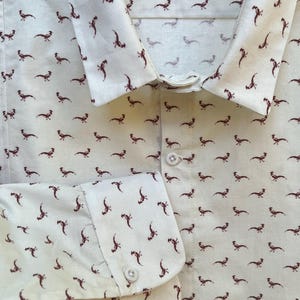 May include: Cream-colored button-down shirt with a repeating pattern of brown pheasant illustrations. The shirt features a classic collar, buttoned cuffs, and a front button closure. The fabric appears to be lightweight.