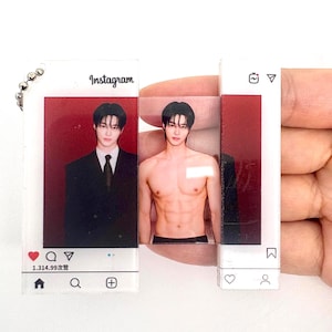 May include: A rectangular acrylic keyring featuring a sliding panel design with an Instagram interface overlay. One side shows a person in a suit, while the sliding section reveals the same person shirtless. Includes icons and text like Instagram.
