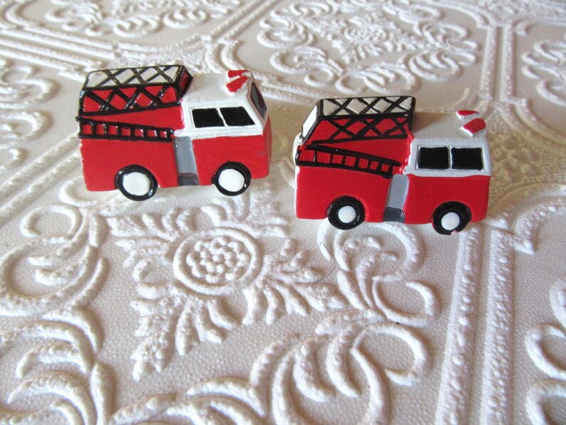 Pu&ograve; includere: Due miniature di autopompe rosse e bianche con dettagli neri. Ogni camion ha una scala, ruote nere e un tetto bianco. Lo sfondo &egrave; una superficie bianca strutturata.