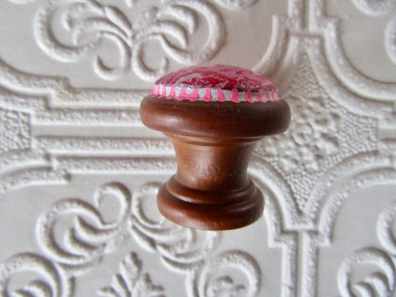 K&ouml;nnte beinhalten: Dekorativer Schrankknopf aus Holz mit dunkelbraunem Finish. Der Knopf hat eine runde Oberseite mit einem rosa und roten Design, akzentuiert mit wei&szlig;en und rosa Zierleisten. F&uuml;r M&ouml;bel und Heimdekoration.