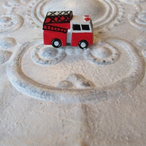Pu&ograve; includere: Un piccolo camion dei pompieri rosso e bianco con ruote nere e una scala sulla parte superiore. Il giocattolo &egrave; posto su uno sfondo bianco strutturato con motivi ornamentali.