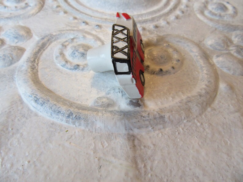 Pu&ograve; includere: Pomello per armadio a forma di camion dei pompieri rosso e bianco con dettagli neri. Il pomello presenta un design a scala e ruote nere. Il pomello &egrave; montato su una base bianca.