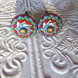 May include: Two decorative cabinet knobs with a colorful geometric design. Each knob features a blue center with a starburst pattern, surrounded by red, green, and yellow accents. The knobs have a brass-colored metal base.
