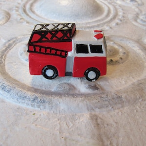 Pu&ograve; includere: Un piccolo camion dei pompieri rosso e bianco con ruote nere e una scala sul tetto. Il camion giocattolo ha un tetto bianco e una griglia nera. Il camion dei pompieri &egrave; un oggetto decorativo.