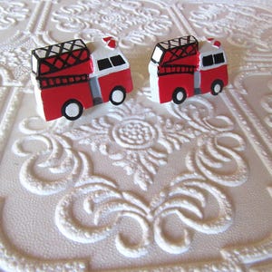 Pu&ograve; includere: Due orecchini a forma di camion dei pompieri rossi e bianchi con dettagli neri e bianchi. Gli orecchini sono repliche in miniatura di camion dei pompieri, con scale e sirene. Sfondo bianco strutturato.