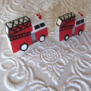 Pu&ograve; includere: Due camion dei pompieri in miniatura dipinti a mano. Ogni camion &egrave; rosso con tetto bianco, scala nera e ruote bianche e nere. Lo sfondo &egrave; una superficie bianca strutturata con un motivo floreale.