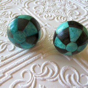 Può includere: Due oggetti decorativi rotondi con un motivo a scacchiera in verde acqua e nero. Gli oggetti sono su una superficie bianca strutturata con un motivo floreale.