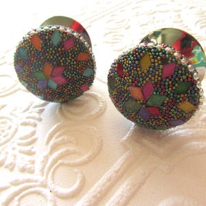 May include: Two decorative cabinet knobs with a mosaic design. The knobs are round with a beaded surface in various colours, including green, orange, pink, and yellow. The knobs have a metallic base and are set against a white background.
