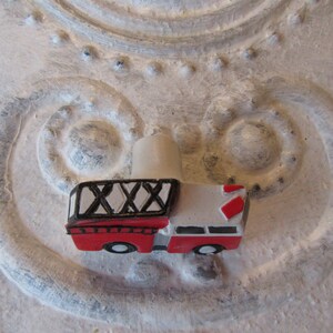 Pu&ograve; includere: Figurina di un piccolo camion dei pompieri rosso e bianco, con dettagli della scala in bianco e nero e un camino beige chiaro. Il giocattolo &egrave; posto su uno sfondo strutturato bianco sporco con motivi a spirale.