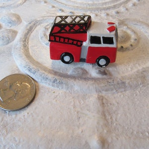 Pu&ograve; includere: Un camioncino dei pompieri rosso e bianco in miniatura con ruote nere, una scala e una sirena. Il giocattolo &egrave; accanto a una moneta. Il camioncino &egrave; un piccolo oggetto decorativo.