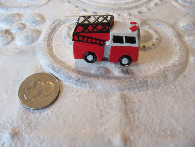 Pu&ograve; includere: Un camioncino dei pompieri rosso e bianco in miniatura con ruote nere, una scala e una sirena. Il giocattolo &egrave; accanto a una moneta. Il camioncino &egrave; un piccolo oggetto decorativo.