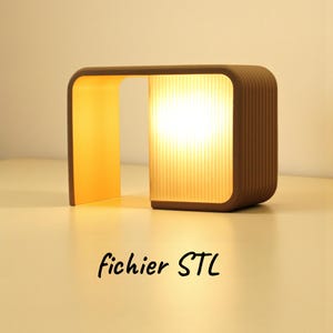 Könnte beinhalten: Eine braune, moderne Lampe mit einem rechteckigen, gerippten Schirm und einer geschwungenen Oberseite. Die Lampe strahlt ein warmes, gelbes Licht aus. Der Text "fichier STL" ist unten in schwarzer Schrift geschrieben.