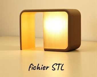 Pode incluir: Uma lâmpada castanha, de estilo moderno, com uma sombra retangular e canelada e um topo curvo. A lâmpada emite uma luz amarela quente. O texto "fichier STL" está escrito em itálico preto na parte inferior.