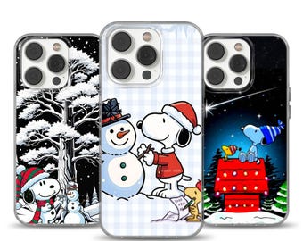Può includere: Tre custodie per telefono con Snoopy e Woodstock in scene invernali. Una custodia mostra Snoopy che costruisce un pupazzo di neve, un'altra Snoopy in una foresta innevata, e la terza Snoopy sulla sua cuccia sotto un cielo stellato.