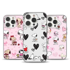 May include: Three phone cases featuring Snoopy and Woodstock designs. The cases have pink and white backgrounds with hearts and Snoopy illustrations. The cases are designed to fit a smartphone.