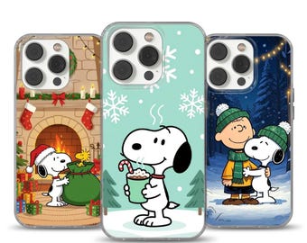 Può includere: Tre custodie per telefono con Snoopy e Charlie Brown in scene invernali. Una custodia mostra Snoopy vicino a un camino, un'altra Snoopy con una bevanda calda, e la terza Charlie Brown e Snoopy che si abbracciano nella neve.