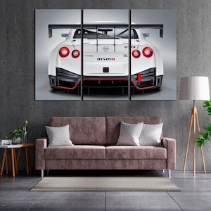 May include: A triptych canvas print featuring the rear view of a white Nissan GT-R Nismo sports car. The car has red accents, a large spoiler, and the Nismo logo. The artwork is displayed above a brown sofa.