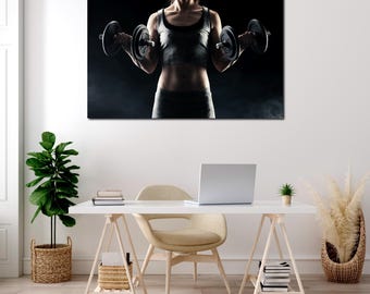 May include: A canvas print showing a person holding two black dumbbells. The person is wearing a grey vest and shorts. The background is dark with a smoky effect. The image is displayed on a white wall above a desk.